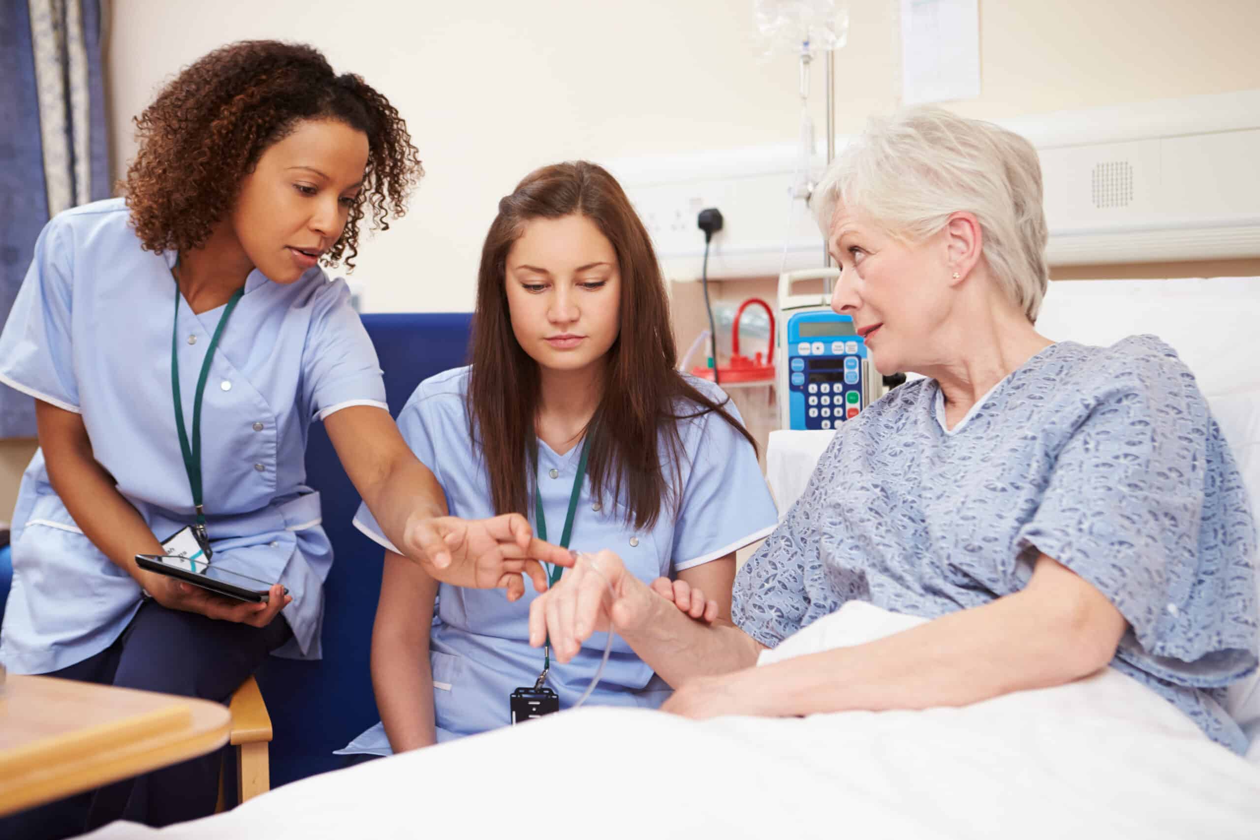 trainee nurse sitting by female patient's bed in hospital