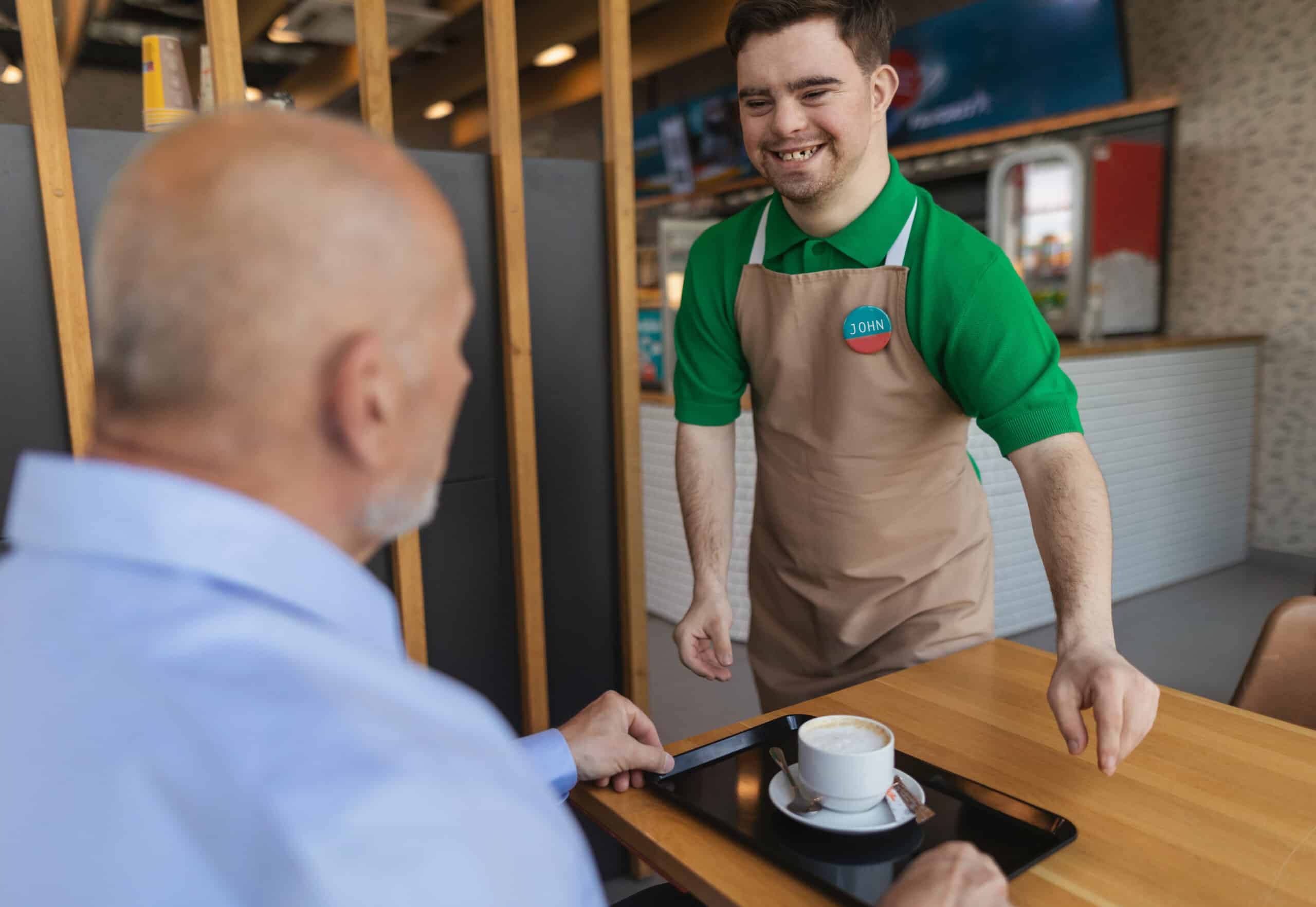 happy waiter with down syndrome serving coffee to senior customer at cafe.