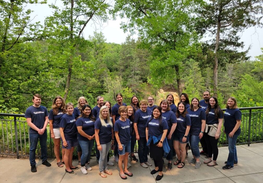 a group of people posing for a photo in front of trees at a scenic location.